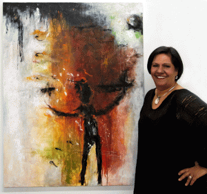 Alicia H. Torres at her studio. Background: Rain of Fish, 2010, mixed media on canvas, 36” x 48”. Photo Gary Mercer garymercerphoto.com © 2010. 